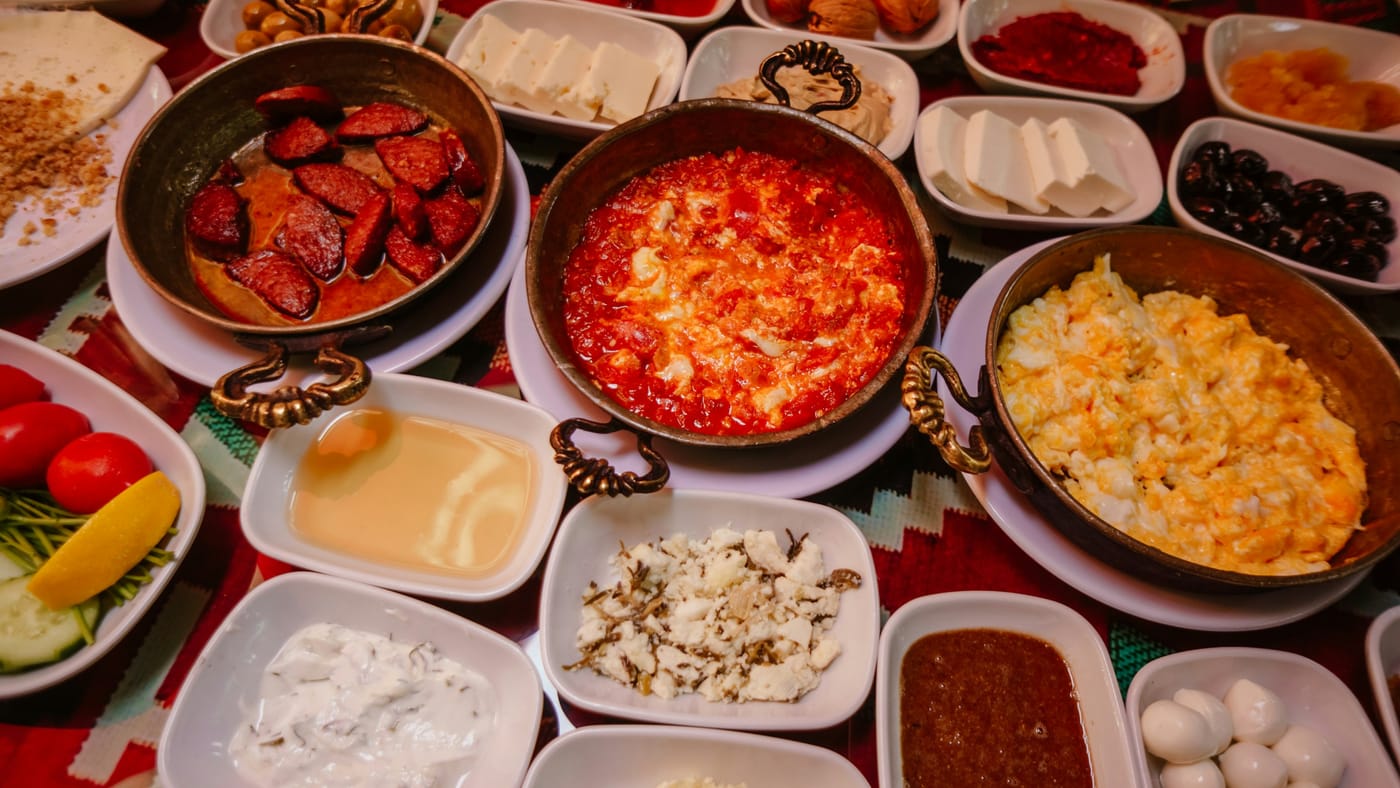 Serpme kahvaltı sofrası: bakır sahanlarda menemen ve sucuklu yumurta, peynir, zeytin ve reçel tabakları