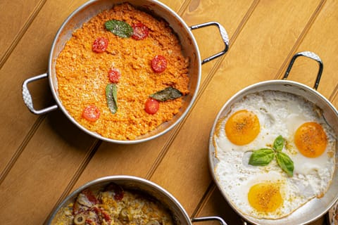 Ahşap masada sahanda menemen ve yanında sahanda yumurta, üstten görünüm